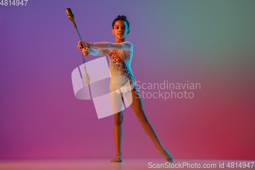 Image of African-american rhythmic gymnast, pretty girl practicing on gradient studio background in neon light