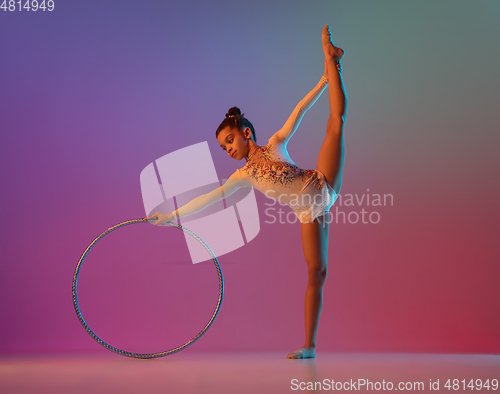 Image of African-american rhythmic gymnast, pretty girl practicing on gradient studio background in neon light