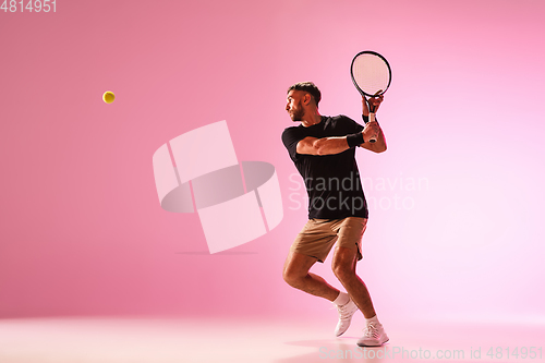 Image of Young caucasian man playing tennis isolated on pink studio background, action and motion concept