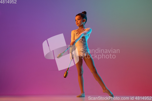 Image of African-american rhythmic gymnast, pretty girl practicing on gradient studio background in neon light