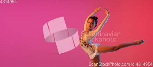 Image of African-american rhythmic gymnast, pretty girl practicing on gradient studio background in neon light