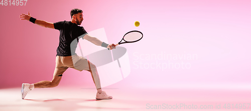 Image of Young caucasian man playing tennis isolated on pink studio background, action and motion concept