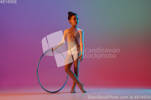 Image of African-american rhythmic gymnast, pretty girl practicing on gradient studio background in neon light