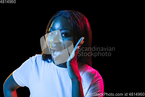 Image of African young woman\'s portrait on dark studio background in neon. Concept of human emotions, facial expression, youth, sales, ad.