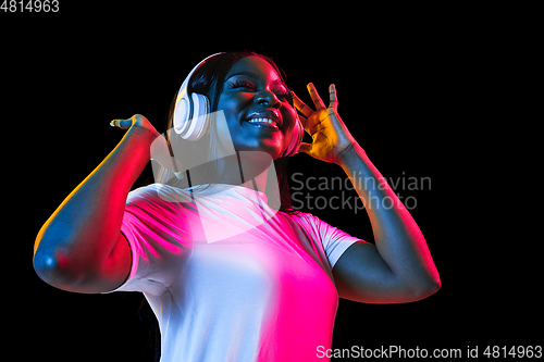 Image of African young woman\'s portrait on dark studio background in neon. Concept of human emotions, facial expression, youth, sales, ad.
