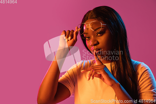Image of African young woman\'s portrait on pink studio background in neon. Concept of human emotions, facial expression, youth, sales, ad.