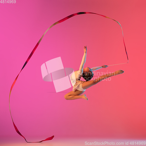 Image of African-american rhythmic gymnast, pretty girl practicing on gradient studio background in neon light