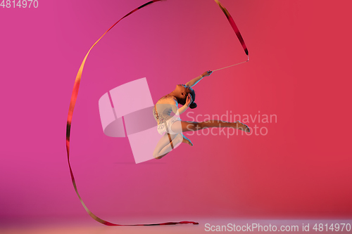 Image of African-american rhythmic gymnast, pretty girl practicing on gradient studio background in neon light