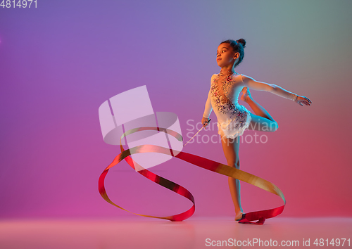 Image of African-american rhythmic gymnast, pretty girl practicing on gradient studio background in neon light