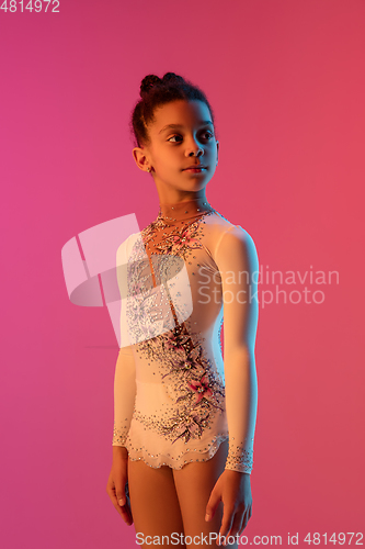 Image of African-american rhythmic gymnast, pretty girl practicing on gradient studio background in neon light