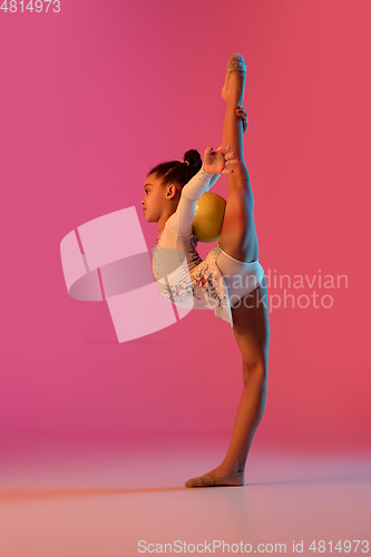 Image of African-american rhythmic gymnast, pretty girl practicing on gradient studio background in neon light