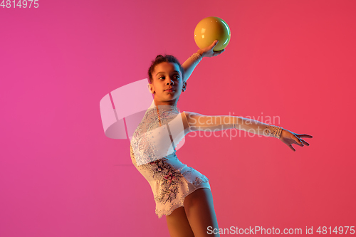 Image of African-american rhythmic gymnast, pretty girl practicing on gradient studio background in neon light