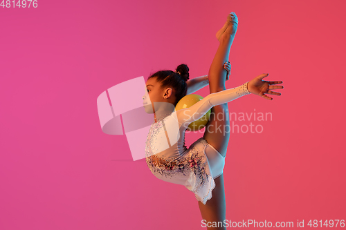 Image of African-american rhythmic gymnast, pretty girl practicing on gradient studio background in neon light