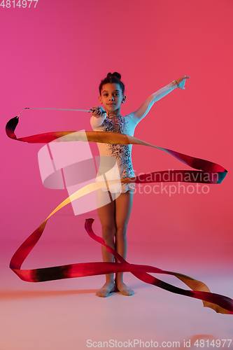 Image of African-american rhythmic gymnast, pretty girl practicing on gradient studio background in neon light