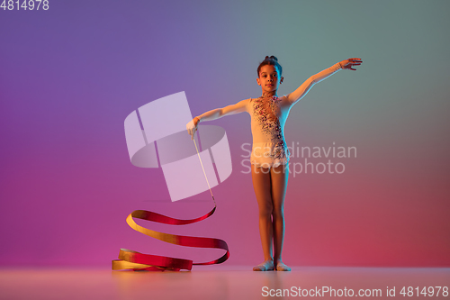 Image of African-american rhythmic gymnast, pretty girl practicing on gradient studio background in neon light