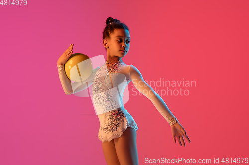 Image of African-american rhythmic gymnast, pretty girl practicing on gradient studio background in neon light