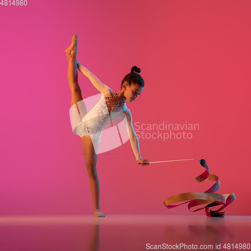 Image of African-american rhythmic gymnast, pretty girl practicing on gradient studio background in neon light