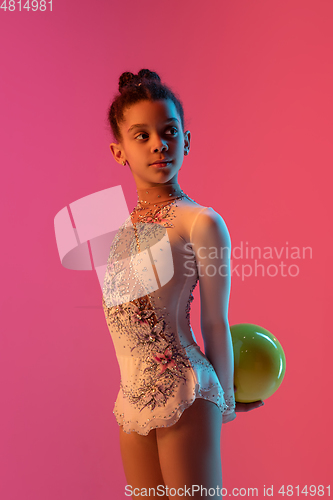 Image of African-american rhythmic gymnast, pretty girl practicing on gradient studio background in neon light