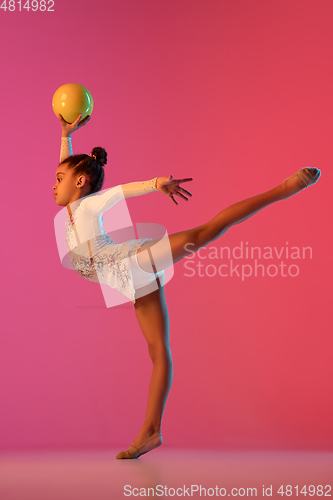 Image of African-american rhythmic gymnast, pretty girl practicing on gradient studio background in neon light