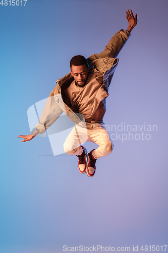 Image of Young stylish man in modern street style outfit isolated on gradient background in neon light. African-american fashionable model in look book, musician performing.