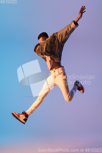 Image of Young stylish man in modern street style outfit isolated on gradient background in neon light. African-american fashionable model in look book, musician performing.