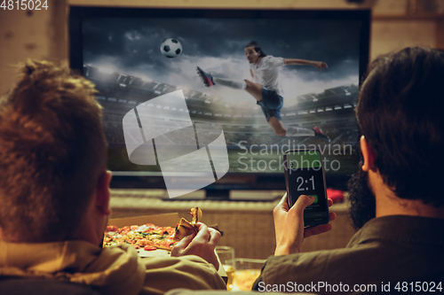 Image of Men with betting application in phone. Group of friends watching TV, sport match together. Emotional fans cheering for favourite team, watching on exciting game.