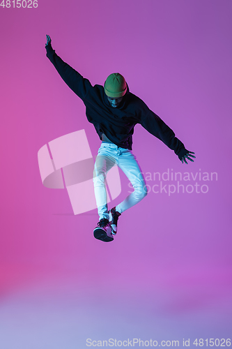 Image of Young stylish man in modern street style outfit isolated on gradient background in neon light. African-american fashionable model in look book, musician performing.