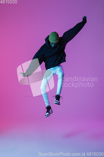 Image of Young stylish man in modern street style outfit isolated on gradient background in neon light. African-american fashionable model in look book, musician performing.