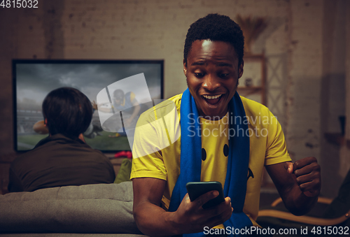 Image of Man with betting application in phone. Group of friends watching TV, sport match together. Emotional fans cheering for favourite team, watching on exciting game.