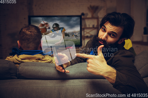 Image of Man with betting application in phone. Group of friends watching TV, sport match together. Emotional fans cheering for favourite team, watching on exciting game.