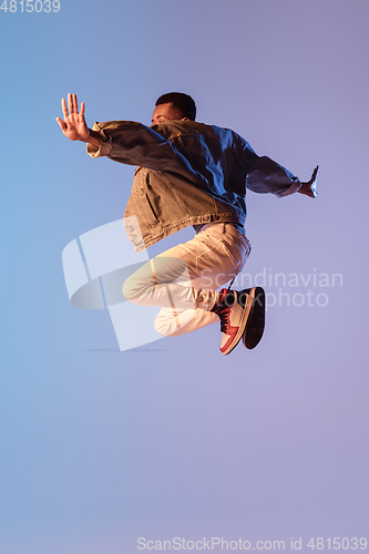 Image of Young stylish man in modern street style outfit isolated on gradient background in neon light. African-american fashionable model in look book, musician performing.