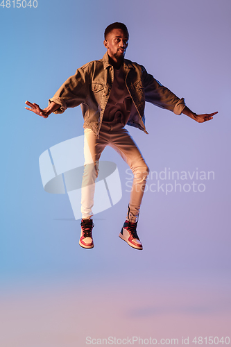 Image of Young stylish man in modern street style outfit isolated on gradient background in neon light. African-american fashionable model in look book, musician performing.