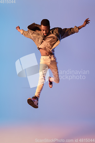 Image of Young stylish man in modern street style outfit isolated on gradient background in neon light. African-american fashionable model in look book, musician performing.
