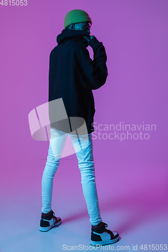 Image of Young stylish man in modern street style outfit isolated on gradient background in neon light. African-american fashionable model in look book, musician performing.