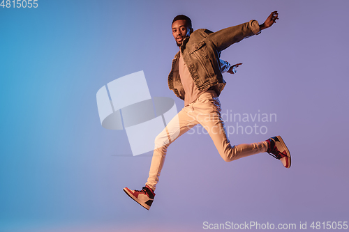 Image of Young stylish man in modern street style outfit isolated on gradient background in neon light. African-american fashionable model in look book, musician performing.