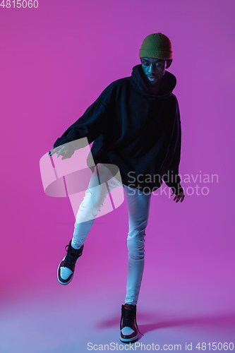 Image of Young stylish man in modern street style outfit isolated on gradient background in neon light. African-american fashionable model in look book, musician performing.