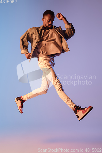 Image of Young stylish man in modern street style outfit isolated on gradient background in neon light. African-american fashionable model in look book, musician performing.