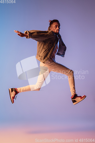 Image of Young stylish man in modern street style outfit isolated on gradient background in neon light. African-american fashionable model in look book, musician performing.