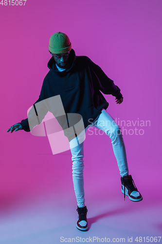 Image of Young stylish man in modern street style outfit isolated on gradient background in neon light. African-american fashionable model in look book, musician performing.