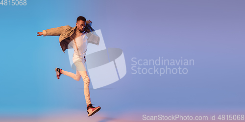 Image of Young stylish man in modern street style outfit isolated on gradient background in neon light. African-american fashionable model in look book, musician performing.