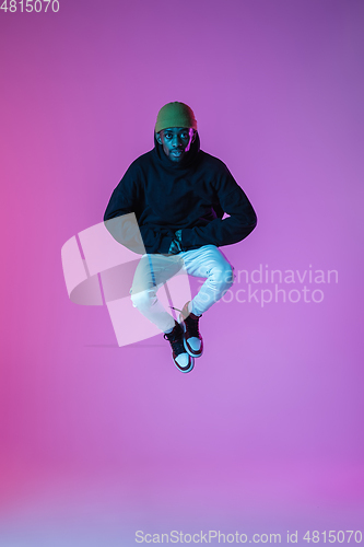 Image of Young stylish man in modern street style outfit isolated on gradient background in neon light. African-american fashionable model in look book, musician performing.