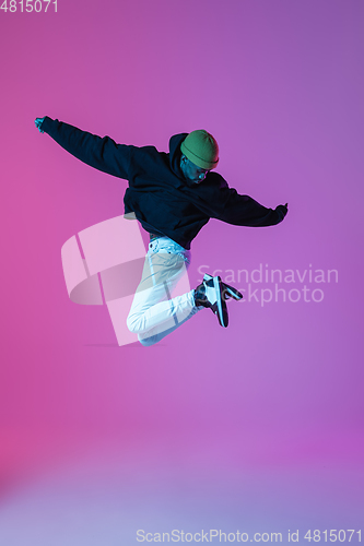 Image of Young stylish man in modern street style outfit isolated on gradient background in neon light. African-american fashionable model in look book, musician performing.