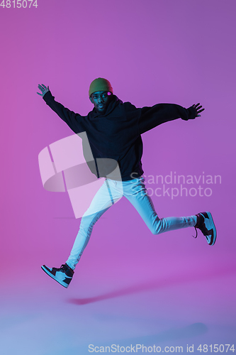 Image of Young stylish man in modern street style outfit isolated on gradient background in neon light. African-american fashionable model in look book, musician performing.