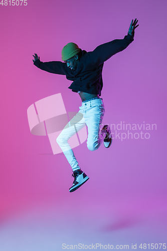 Image of Young stylish man in modern street style outfit isolated on gradient background in neon light. African-american fashionable model in look book, musician performing.