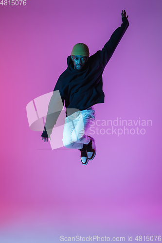 Image of Young stylish man in modern street style outfit isolated on gradient background in neon light. African-american fashionable model in look book, musician performing.