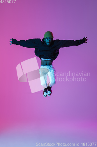 Image of Young stylish man in modern street style outfit isolated on gradient background in neon light. African-american fashionable model in look book, musician performing.