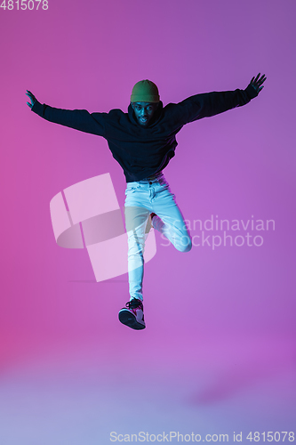 Image of Young stylish man in modern street style outfit isolated on gradient background in neon light. African-american fashionable model in look book, musician performing.