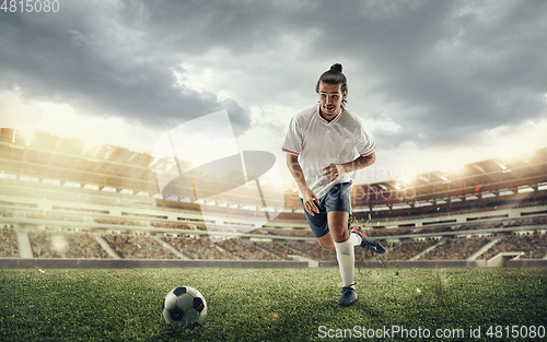 Image of Male soccer, football player catching ball in jump at the stadium during sport match on dark sky background