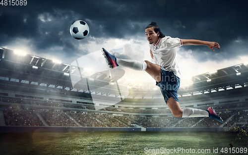 Image of Male soccer, football player catching ball in jump at the stadium during sport match on dark sky background