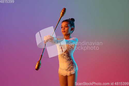 Image of African-american rhythmic gymnast, pretty girl practicing on gradient studio background in neon light